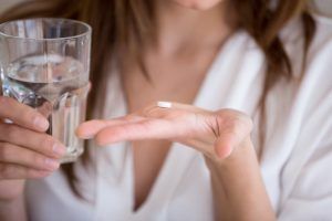 woman holding pill and glass of water